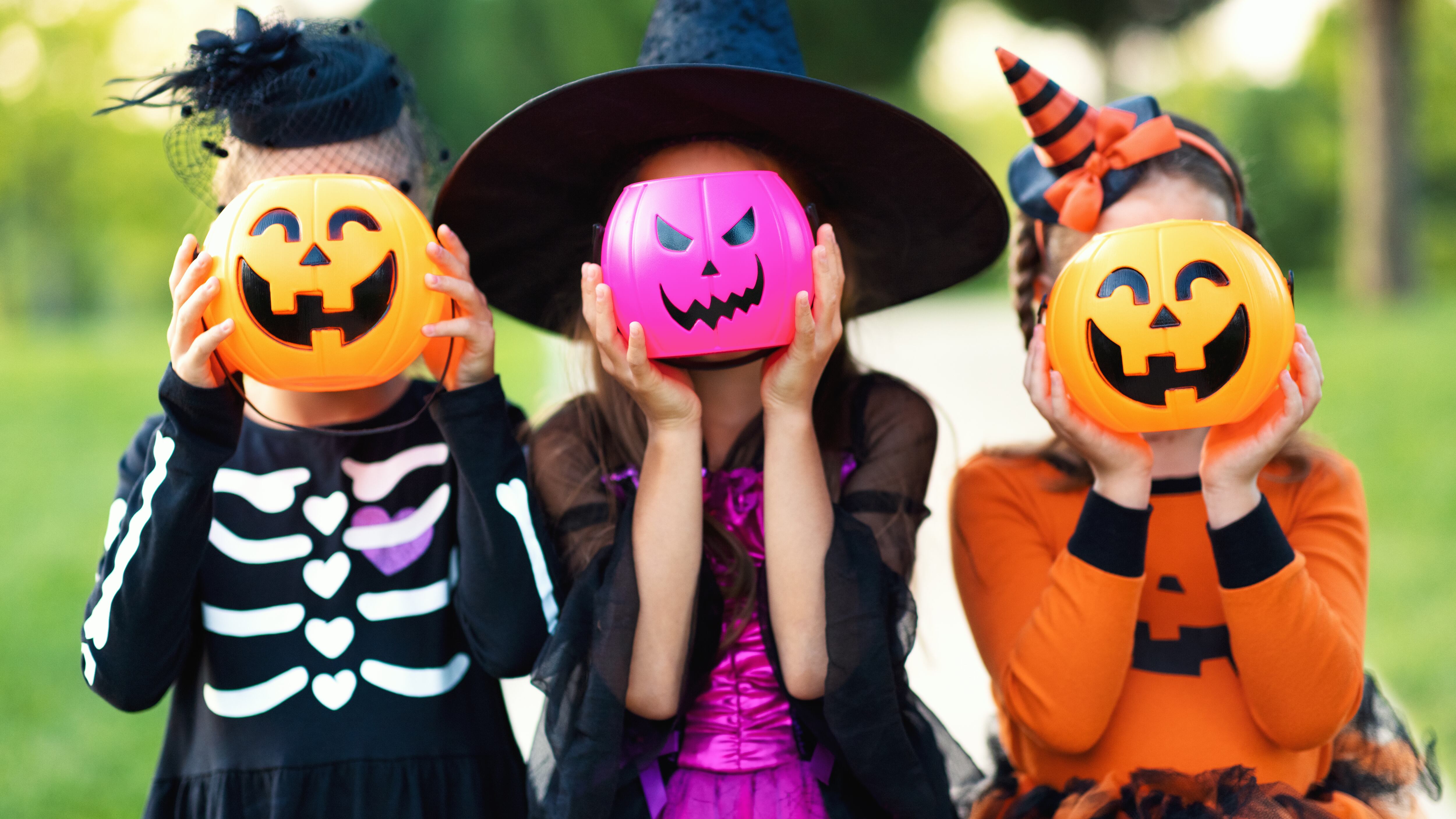 Happy Halloween! funny kids girls in fancy dress hide their heads behind buckets pumpkins outdoors