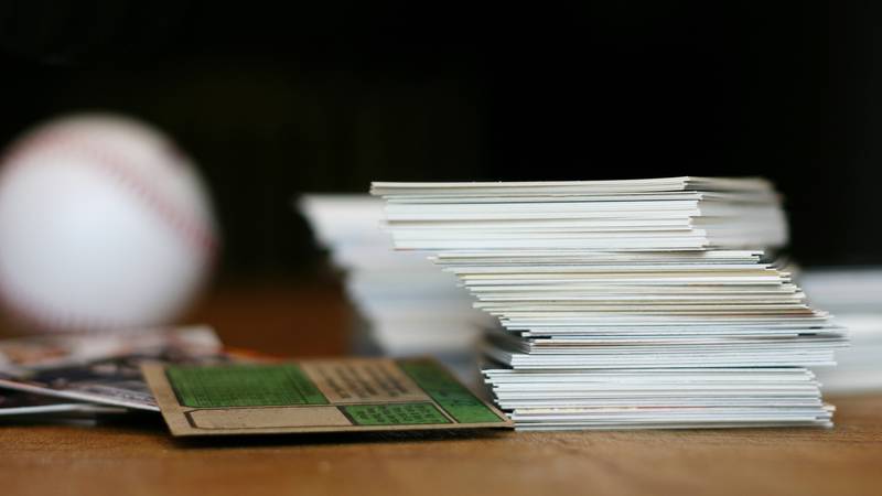 "Collection of baseball cards and baseball on old wooden table.  Shallow dof, focus on stack of cards baseball in background is out of focus."